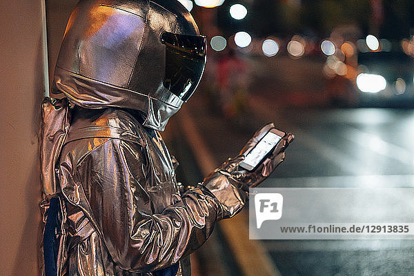 Spaceman at a city street at night using cell phone