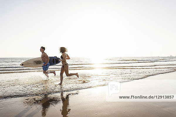 Young couple running on beach  carrying surfboard