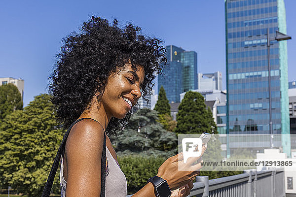 Germany  Frankfurt  smiling young woman with curly hair looking at cell phone