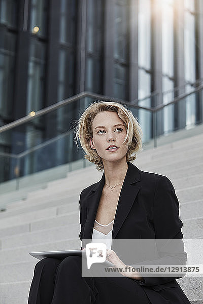 Portrait of blond businesswoman with tablet sitting on stairs outdoors