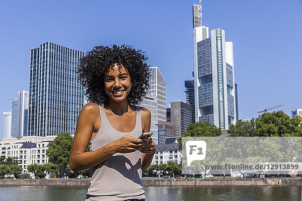 Germany  Frankfurt  portrait of smiling young woman with smartphone in the city