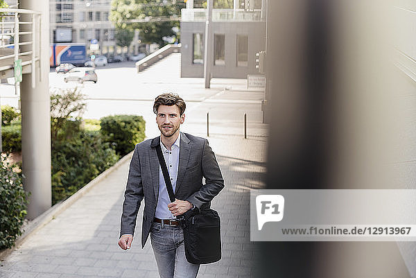 Smiling businessman with crossbody bag in the city on the move