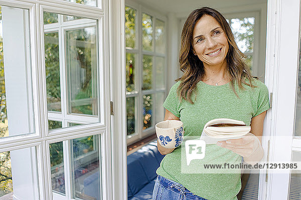 Smiling mature woman at home with book and coffee mug
