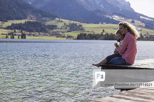 Austria  Tyrol  Walchsee  happy mother and daughter sitting on a jetty at the lake
