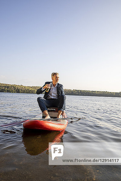 Businessman relaxing with drink on paddleboard on a lake
