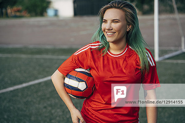 Smiling young woman standing on football ground holding the ball