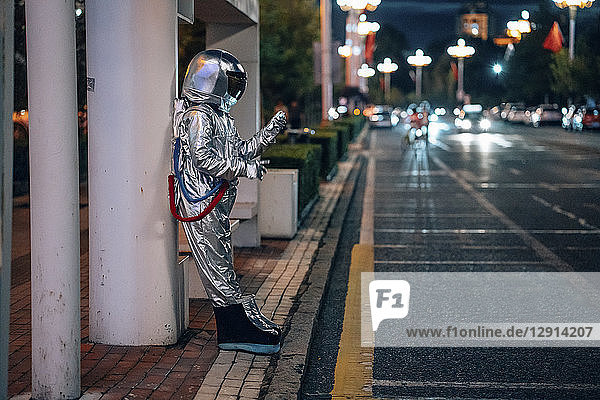 Spaceman standing at a bus stop at night holding cell phone