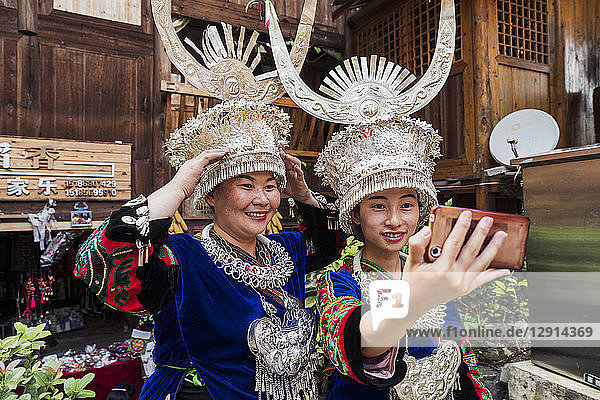 China  Guizhou  two Miao women wearing traditional dresses and headdresses taking a selfie with smartphone