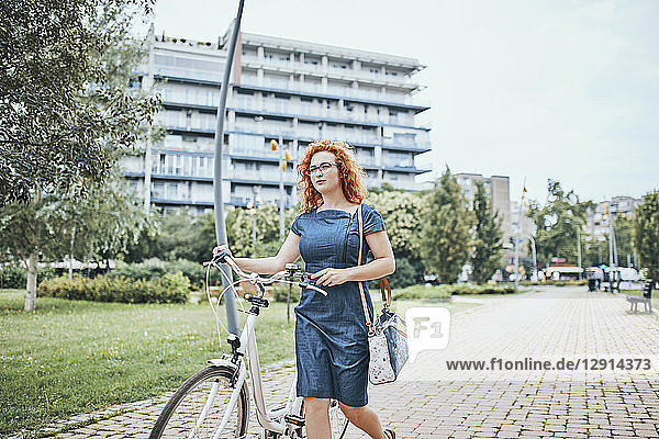 Young woman walking in park  pushing bicycle