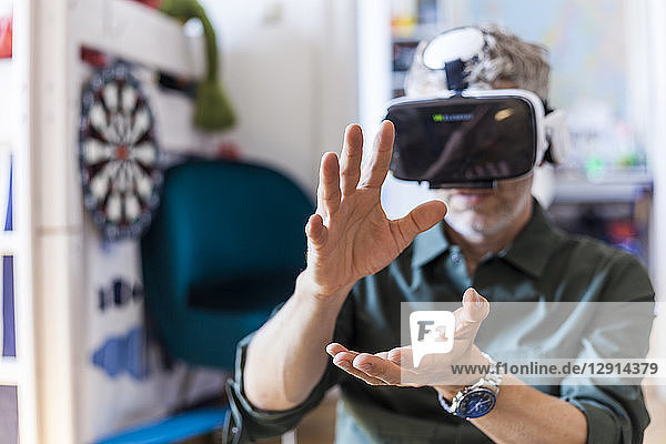 Portrait of mature man at home using Virtual Reality Glasses