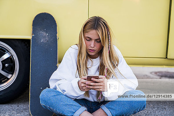 Young woman with skateboard and cell phone sitting at a van