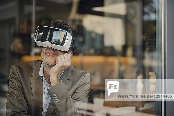 Mature businessman sitting in coffee shop  looking through VR glasses