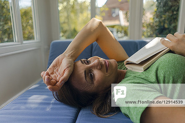 Smiling mature woman lying on couch at home with book
