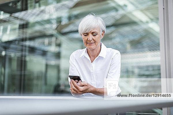 Senior businesswoman leaning on railing in the city looking at cell phone