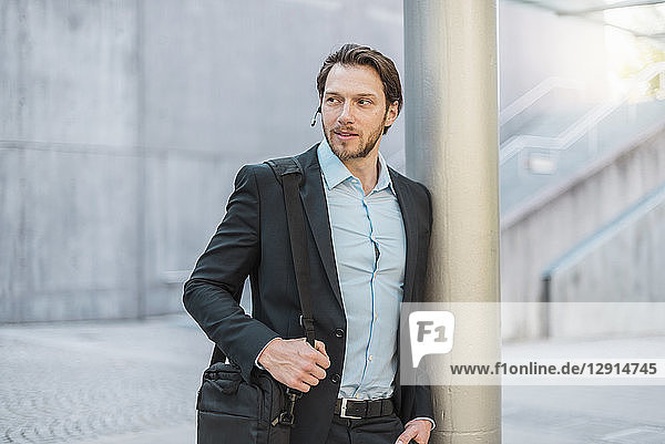 Businessman with laptop bag wearing headset outdoors