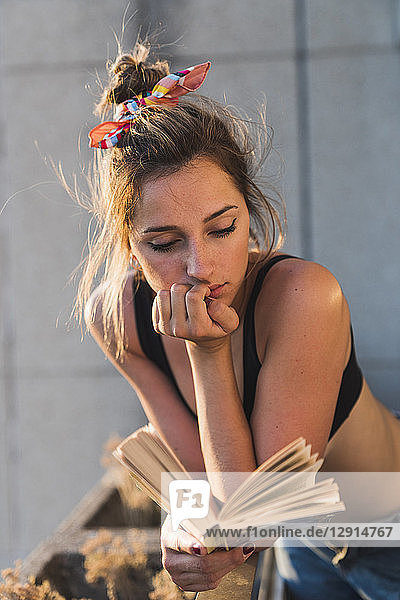 Young woman wearing bra reading book on balcony