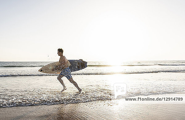 Young man running on beach  carrying surfboard