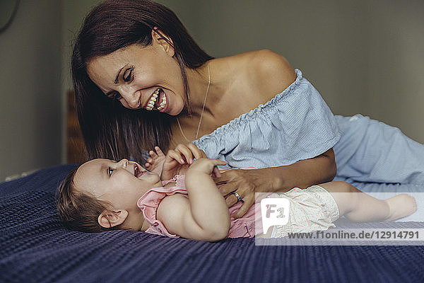Happy mother playing with her baby girl on bed