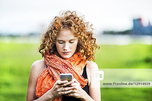 Portrait of young woman with curly red hair looking at cell phone