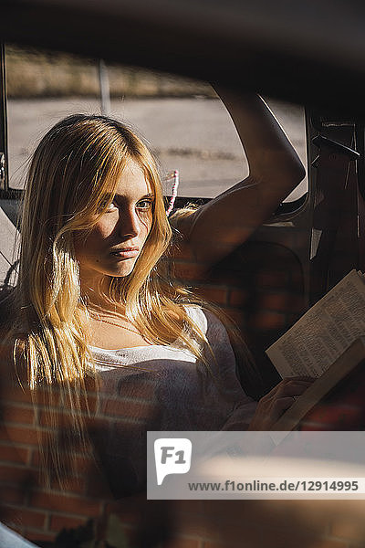 Portrait of young woman sitting in a car reading book