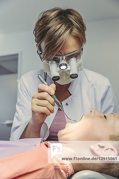Denist examining boy's teeth  using head magnifiers and dental instrument