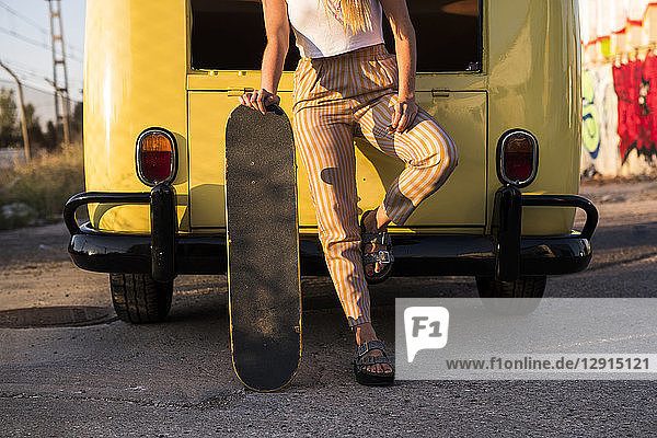 Young woman with skateboard standing outside at a vintage van