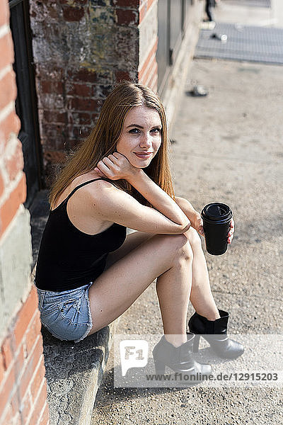 Young woman sitting in the street on a doorstep  holding a cup of coffee