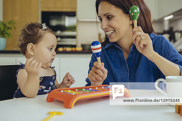 Happy mother and baby daughter playing with rattles