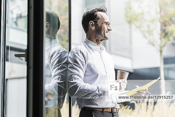 Laughing businessman with papers and coffee to go looking at distance