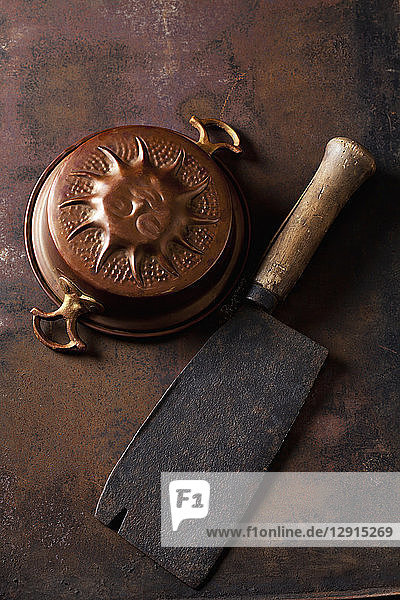 Old copper baking dish and cleaver on rusty ground