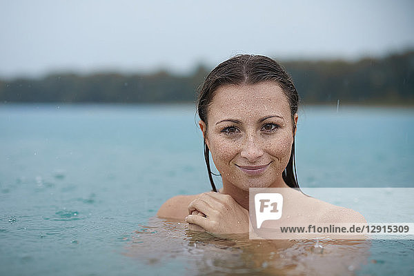 Portrait of smiling young woman bathing in lake on rainy day