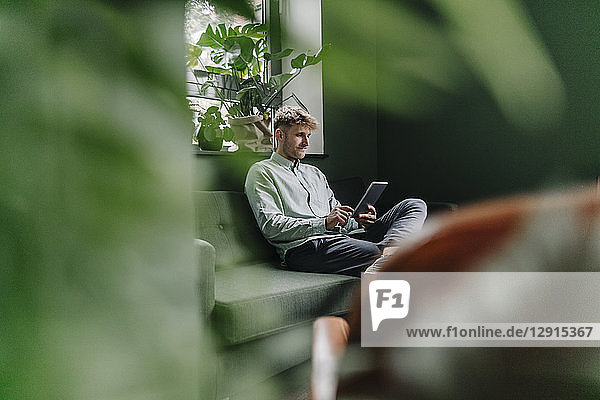 Young man sitting on green couch  using digital tablet