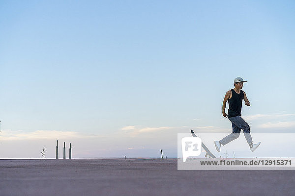 Young man running next to skateboard on a lane at dusk