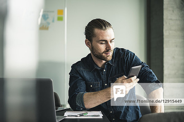 Young businessman sitting in office using cell phone