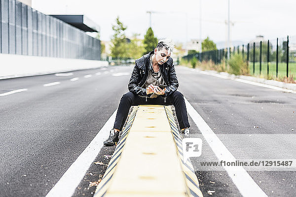 Punk woman sitting at the roadside using cell phone