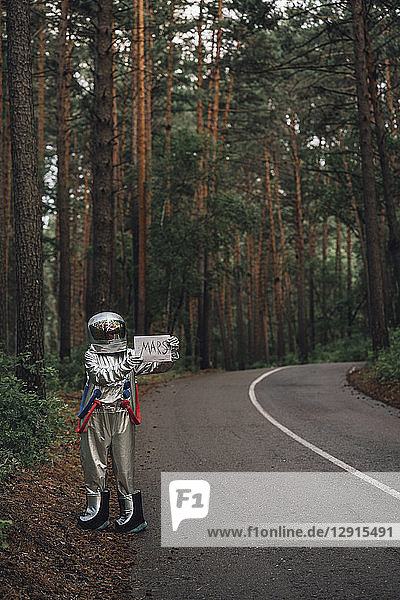 Spaceman hitchhiking to Mars  standing on road in forest