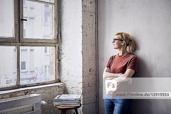 Smiling woman leaning against wall in loft looking through window