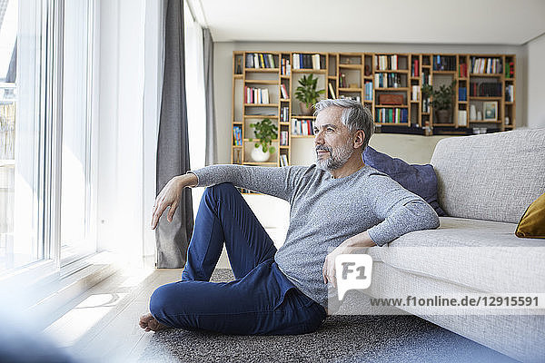 Mature man sitting on floor of his living room looking out of window