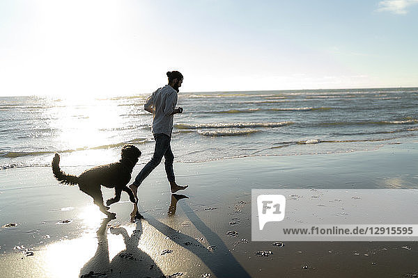 Young man running and playing with his dog on the beach