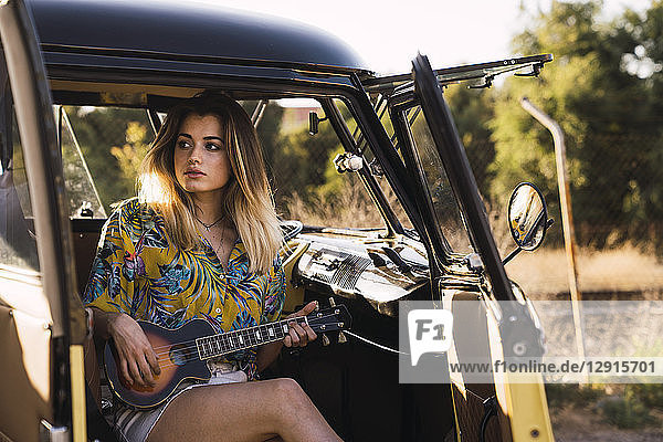Young woman sitting in a van playing guitar