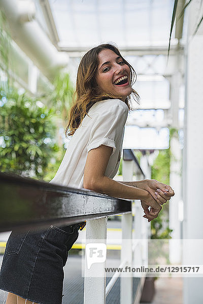 Young woman in greenhouse leaning on railing  laughing  portrait