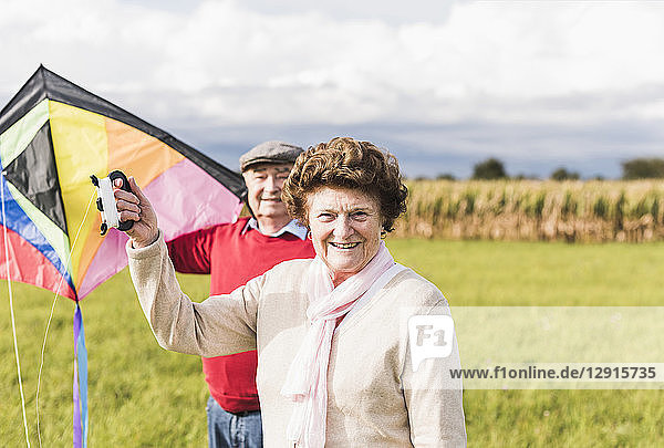 Portrait of smiling senior couple with kite in rural landscape