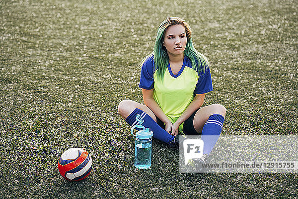 Young woman sitting on football ground with water bottle and ball