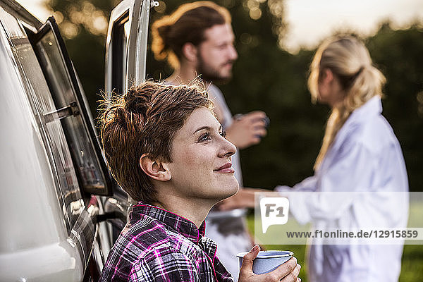 Woman with friends enjoying coffee at a van in rural landscape