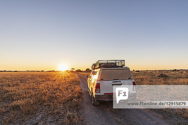 Botswana  Kalahari  Central Kalahari Game Reserve  off-road vehicle on gravel road at sunrise