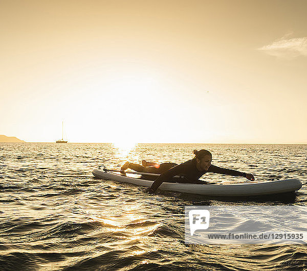 Young woman lying on paddleboard at sunset