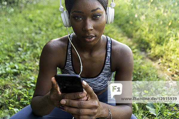 Young athlete in nature  listening music with headphones  holding smartphone