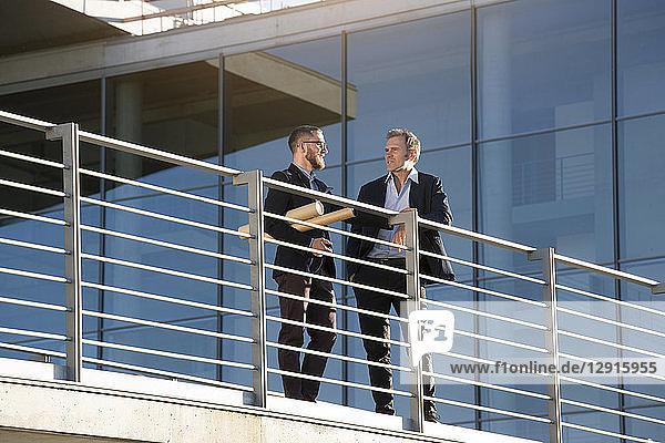 Two businessmen talking on a bridge in the city