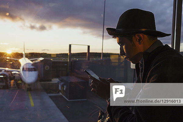 Young man using cell phone at the airport at sunset
