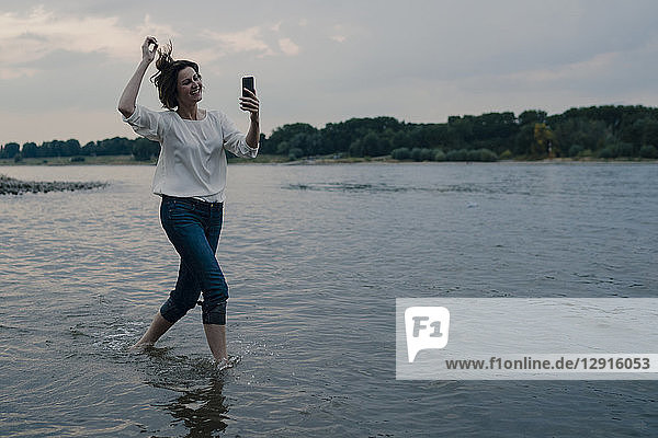 Laughing woman running at the riverside  using smartphone